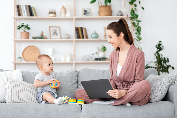 mom sat on a sofa working from home with her toddler son MIN A happy mother working from home sitting on the sofa interacting with her son